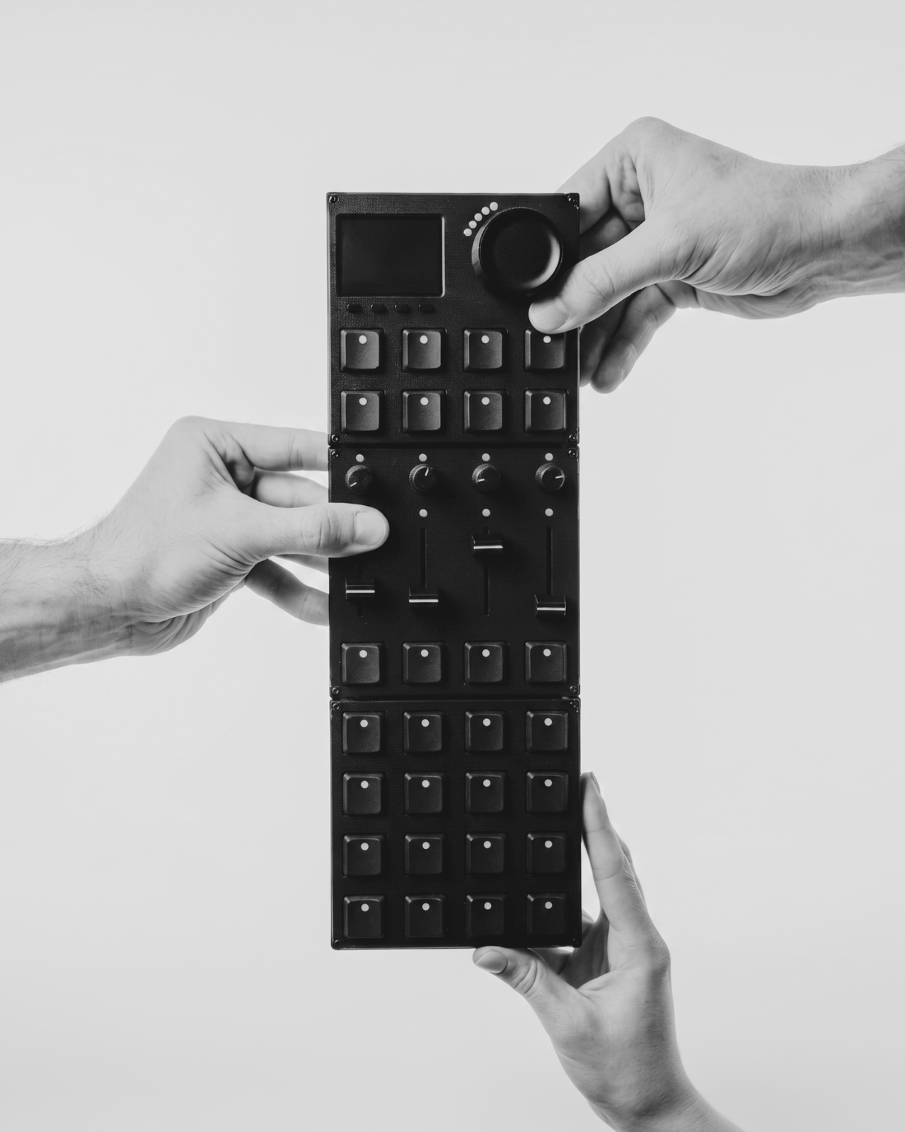 Three hands holding a modular Intech Studio Grid controller stack